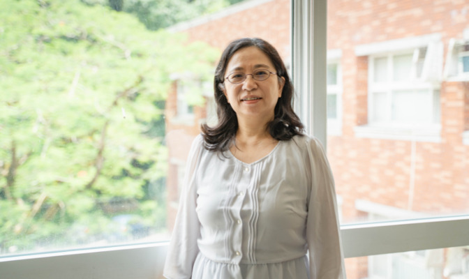 吳佩珍與百年樓旁鳳凰樹合影,象徵文學院的活力與繁盛(攝影:許芷婕)